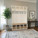 White hall tree with storage baskets in a room with a rug, plant, and table.